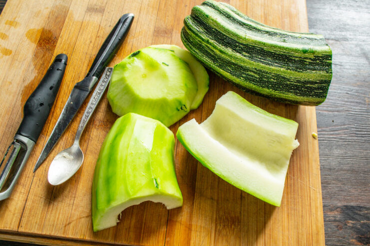 Preparing the Zucchini: Scooping Out the Seeds A hand holding a spoon scooping out seeds from a halved zucchini.