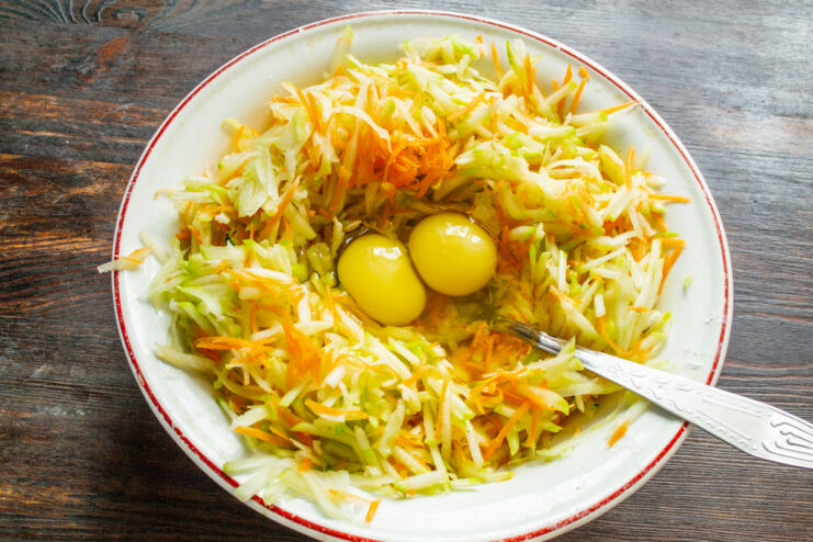 Combining Vegetables with Eggs and Salt Adding two eggs to a bowl of grated zucchini and carrots.