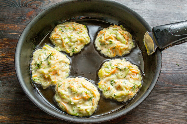 Frying the Draniki: Spooning Batter into the Hot Pan Spoonfuls of zucchini-carrot batter being placed into a hot frying pan with oil.