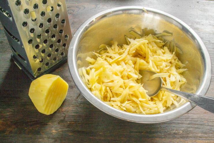 How to Prepare Potatoes for Draniki: Grating on a Coarse Grater A bowl of coarsely grated potatoes, the first step in making draniki.