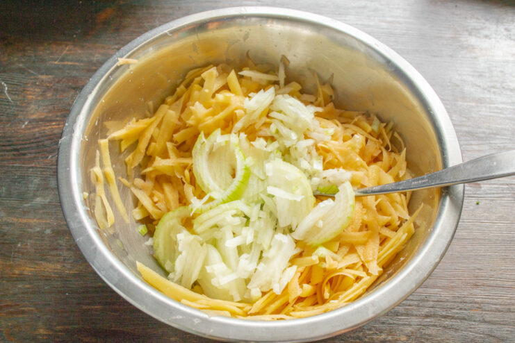 Combining Grated Potatoes and Onions for Potato Pancake Batter A bowl containing a mixture of grated potatoes and finely chopped onions.