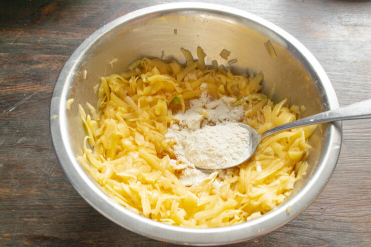 Adding Flour to Bind the Draniki Mixture Adding two tablespoons of wheat flour to the potato and onion mixture in a bowl.