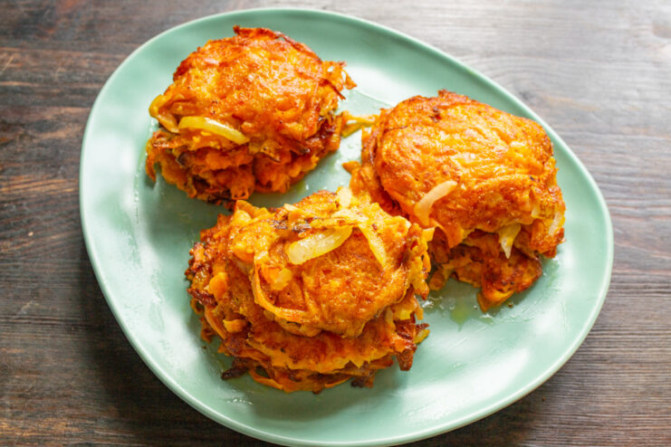 Serving Hot Sweet Potato Draniki with Sauce A stack of freshly fried sweet potato draniki on a plate, served with a side of creamy sauce.