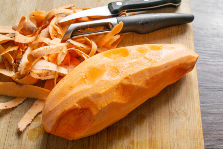 Washing and Peeling the Sweet Potato A whole, unpeeled orange sweet potato next to a peeled one on a cutting board.