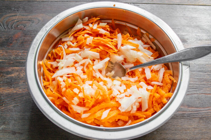 Adding Diced Onion to the Sweet Potato Mixture A bowl with grated sweet potato and finely chopped onions being mixed.