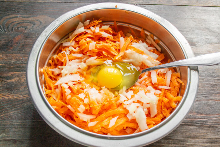 Adding an Egg to Bind the Draniki Batter An egg being cracked into a bowl of grated sweet potato and onion mixture.