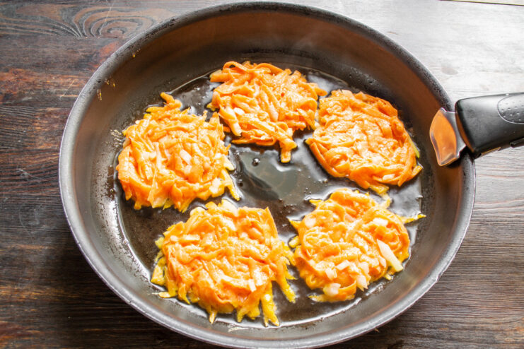 Frying the Sweet Potato Draniki Spoonfuls of sweet potato batter being placed onto a hot, oiled frying pan.