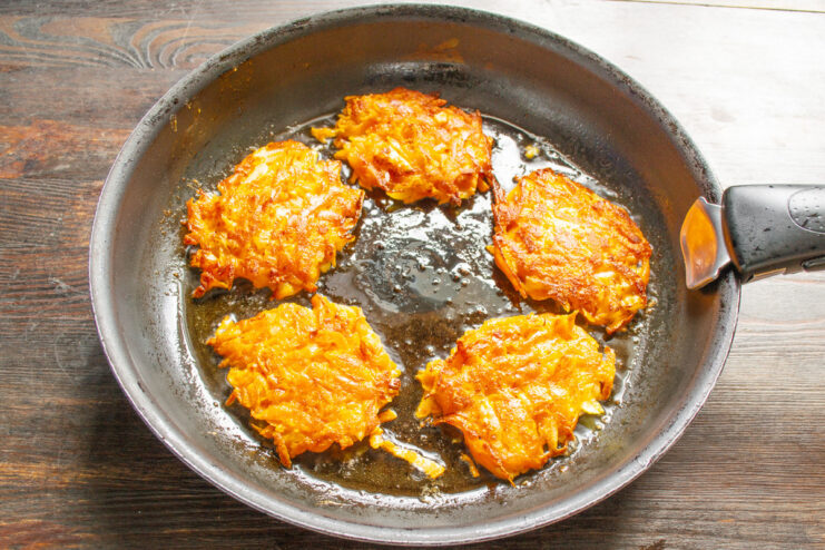 Flipping the Draniki to Cook Until Golden Brown Sweet potato draniki being flipped in a pan, showing a golden-brown cooked side.