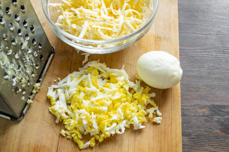 Combining Grated Eggs and Cheese for the Salad A bowl containing grated hard-boiled eggs and grated processed cheese, ready to be mixed.