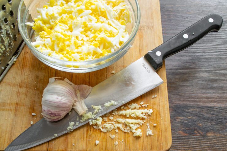 How to Mince Garlic into a Paste for Maximum Flavor A garlic clove being crushed and minced with the flat side of a chef's knife on a cutting board.