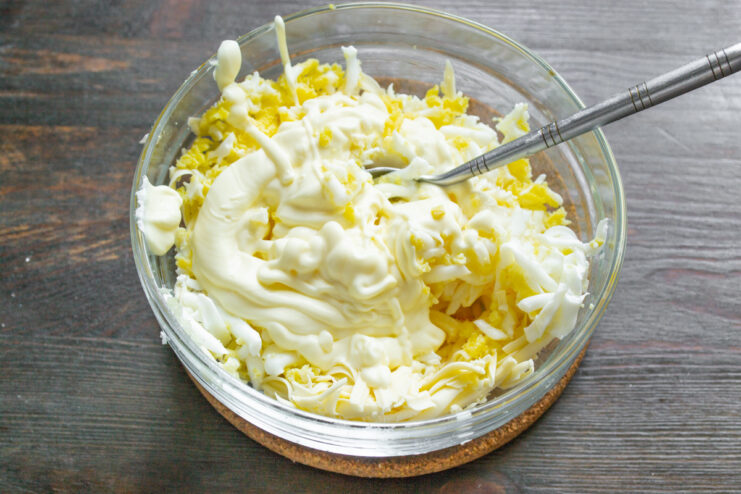 Adding Mayonnaise to Bind the Salad Ingredients Adding a spoonful of mayonnaise to the bowl with grated cheese and eggs.