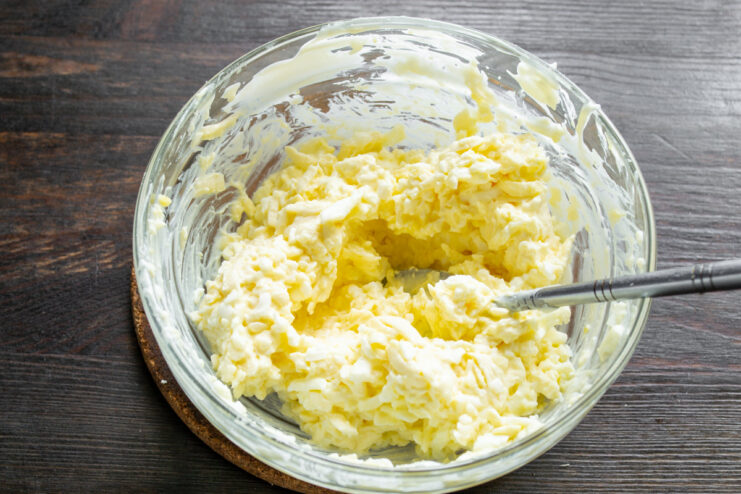 Mixing the Jewish-Style Cheese Salad Until Well Combined A spoon mixing the processed cheese, egg, and mayonnaise salad in a bowl.