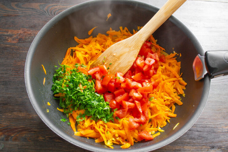 Adding Diced Tomatoes to the Sautéed Vegetables Adding diced tomatoes to sautéed onions and carrots in a skillet.