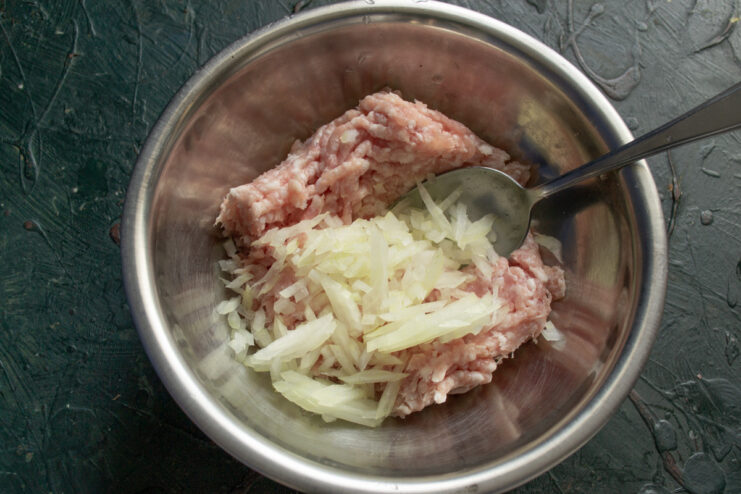Adding Finely Chopped Onion to the Meat Filling Adding finely chopped onion to a bowl of minced meat for the stuffing.