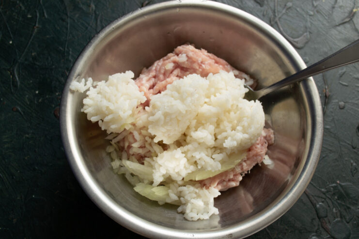 Combining Cooked Rice with the Meat and Onion Mixture Adding cooled, cooked rice to the bowl with minced meat and onions.
