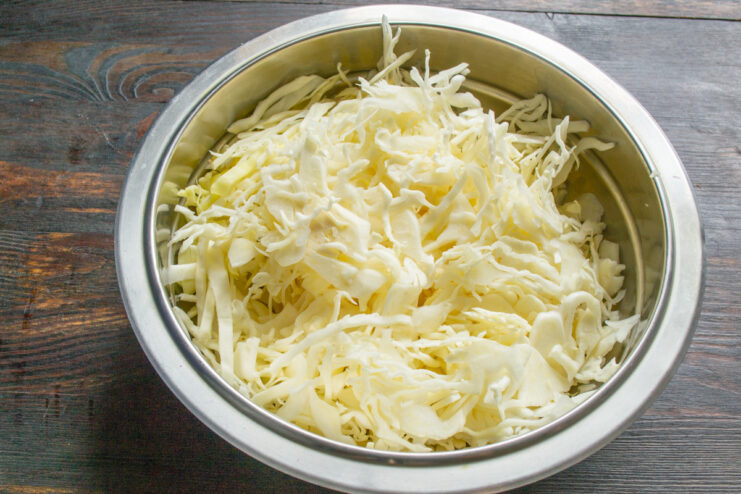 How to Properly Shred Cabbage for Fermentation A close-up of white cabbage being thinly shredded on a cutting board.