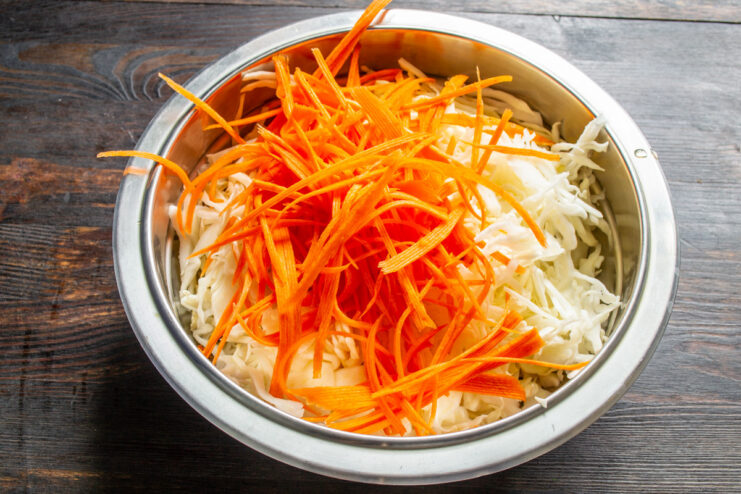 Julienning Carrots for the Perfect Fermented Cabbage Mix A hand using a julienne peeler to slice a carrot into thin strips.