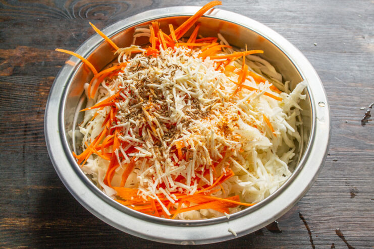 Seasoning the Cabbage Mix with Caraway and Red Pepper Caraway seeds and red pepper flakes being added to the shredded cabbage and carrots.