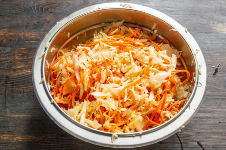 Massaging Vegetables to Release Juices for Fermentation Hands in gloves massaging a mixture of shredded cabbage, carrots, and spices in a large bowl.