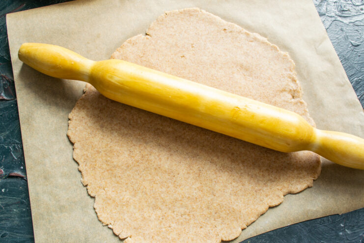 Rolling Out the Dough on Parchment Paper Pie dough being rolled out with a rolling pin on a sheet of parchment paper.