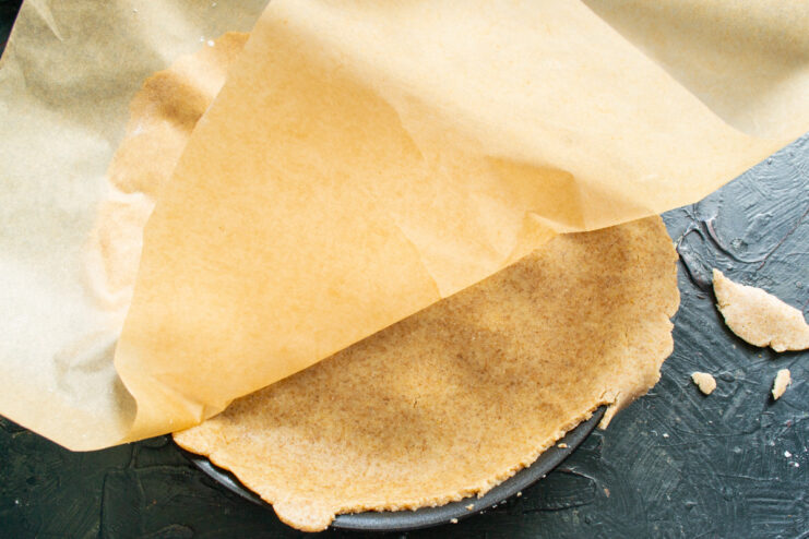 Covering the Apples with the Rolled-Out Dough A sheet of rolled-out dough on parchment paper being placed over the caramelized apples in a skillet.