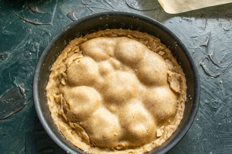 Tucking in the Edges of the Pie Crust Hands tucking the edges of the pie dough into the skillet around the apple filling.