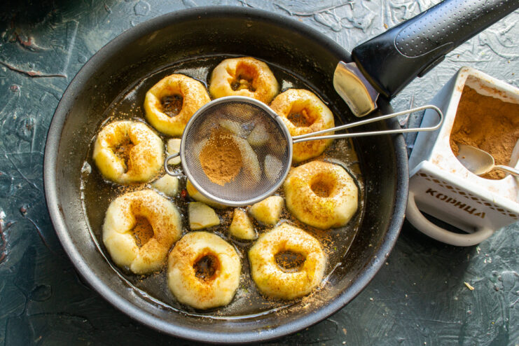 Seasoning the Cooled Caramelized Apples with Cinnamon Caramelized apples in a skillet being sprinkled with ground cinnamon.