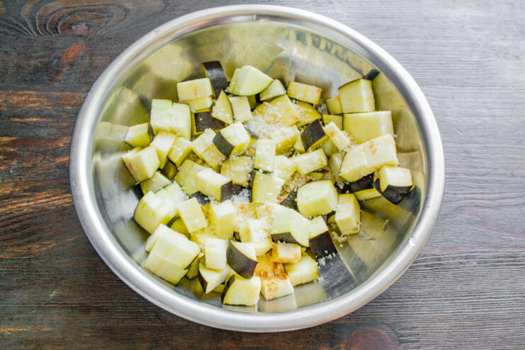A purple eggplant being diced into small cubes on a cutting board.