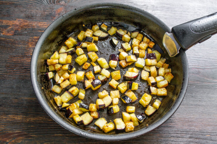 Diced eggplant being fried to a golden-brown color in a hot skillet.