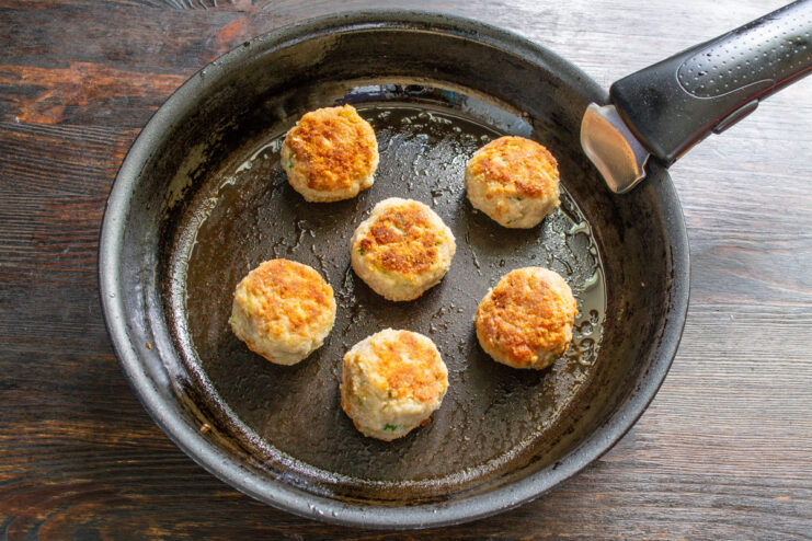Meatballs being fried until golden brown in a hot, oiled skillet.