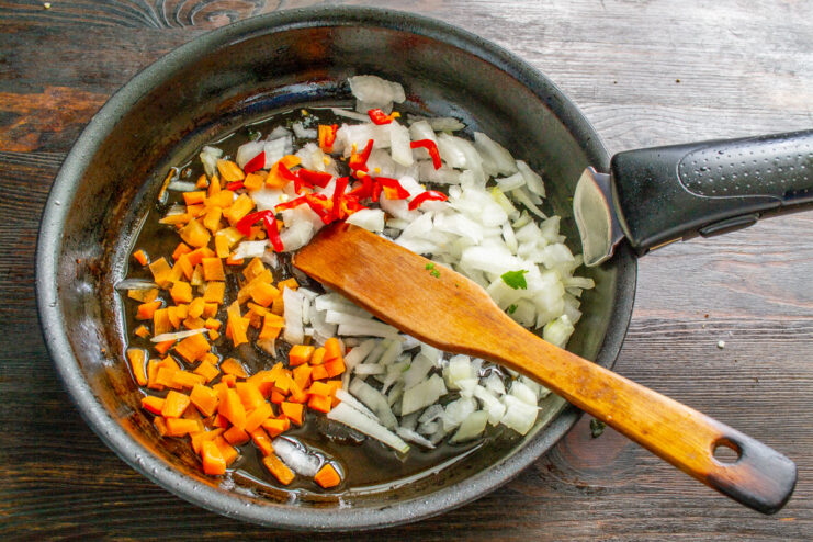 Chopped onions, carrots, and chili peppers being sautéed in a pan.