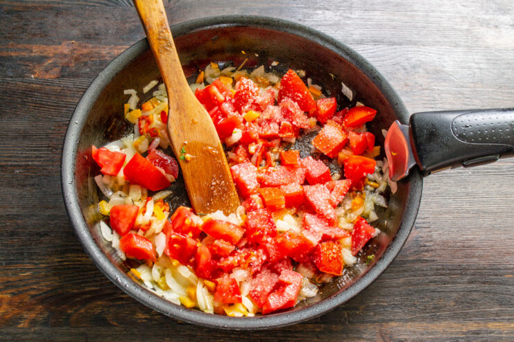 Adding diced bell peppers and tomatoes to the sautéed vegetables in the pan.