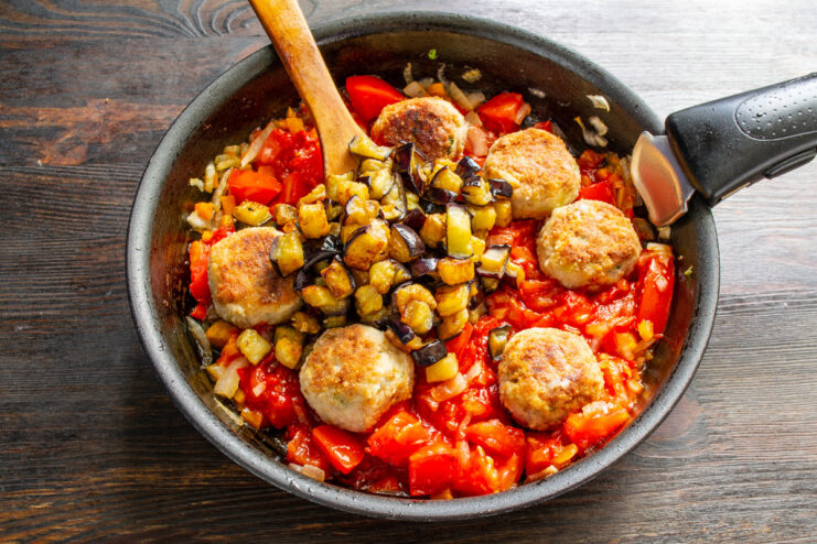 Adding fried eggplant cubes to the pan with meatballs and tomato sauce.