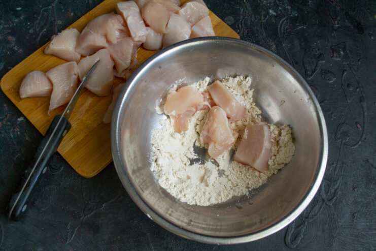 Raw chicken breast being diced into small cubes on a cutting board.