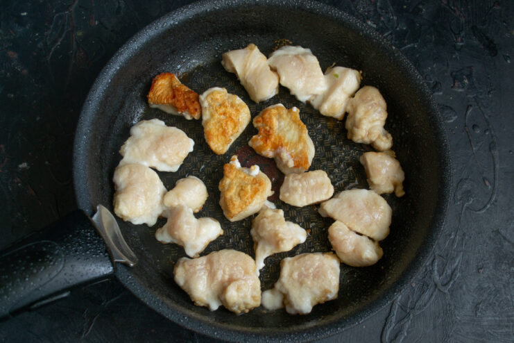 Diced chicken pieces frying in a single layer in a hot skillet.