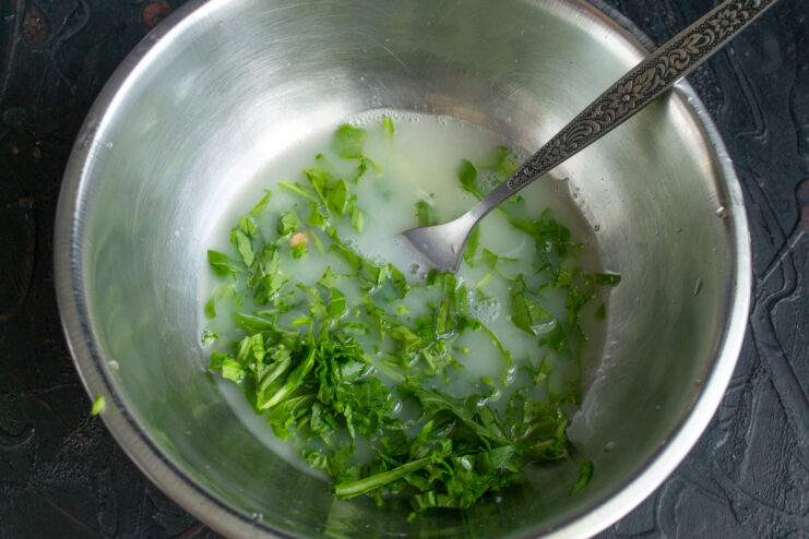 A bowl containing mozzarella brine and chopped arugula, ready for the eggs.