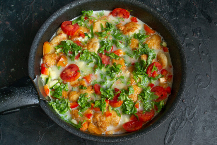The egg mixture being poured from a bowl into the skillet over the cooked chicken and vegetables.