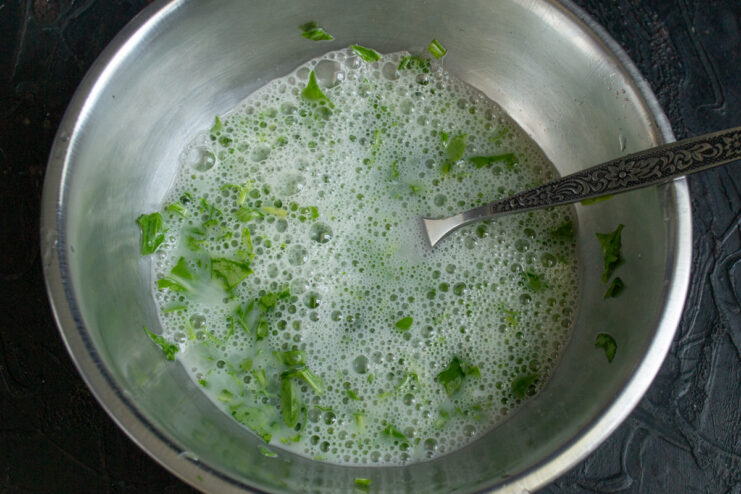 Eggs being cracked into a bowl with arugula and mozzarella brine.