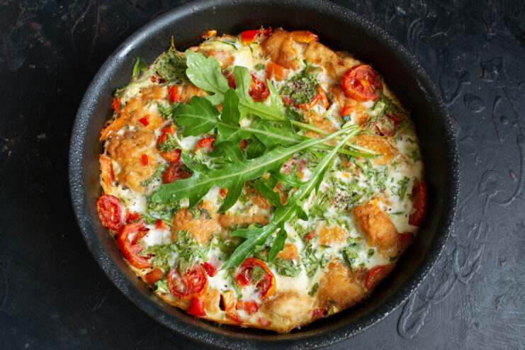 The finished frittata in the skillet, garnished with fresh herbs and black pepper, ready to be served.