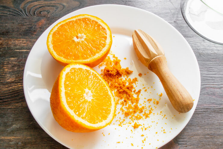 Preparing the orange base: grating zest and squeezing fresh juice for maximum flavor. An orange being zested on a fine grater next to a glass of freshly squeezed orange juice.