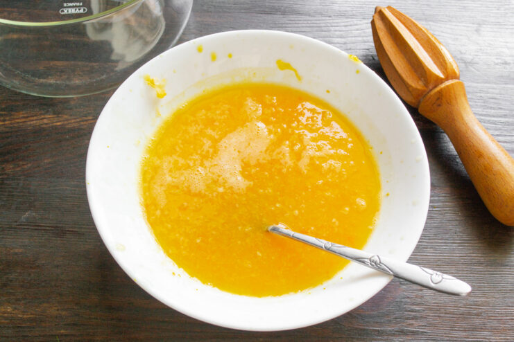 Infusing the orange juice with zest by gently heating it. Orange juice being heated in a small saucepan on a stove.