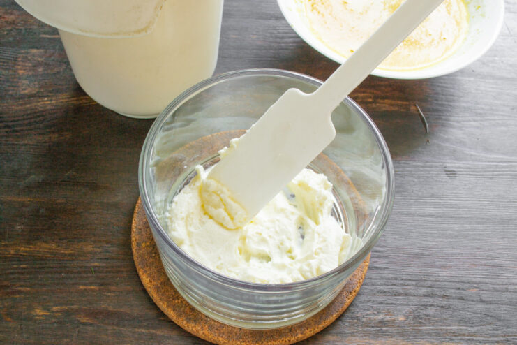 Making the creamy filling: whipping mascarpone, sugar, and heavy cream until fluffy. A bowl with mascarpone and powdered sugar being mixed, with cream being poured in.