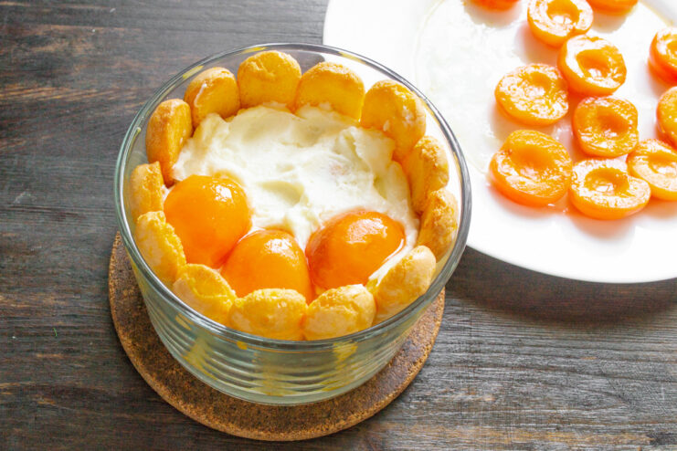 Topping the cake with the cooled, caramelized apricots for a beautiful finish. Placing cooked apricot halves on top of the final cream layer of the cake.