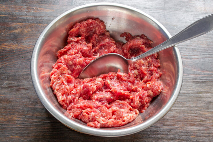 Pro Tip for Juicy Meatballs: Adding Liquid to Ground Beef A bowl of ground beef with a small amount of liquid being added to it.