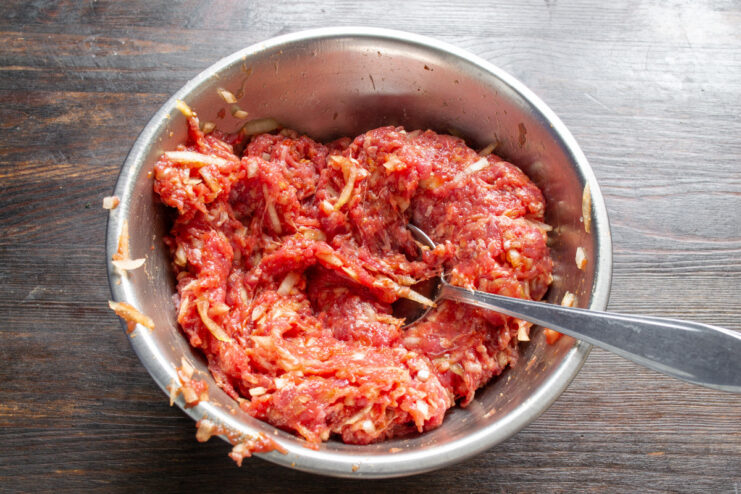 Mixing the Ground Beef Mixture for Even Flavor Hands mixing ground beef with onions and spices in a glass bowl.