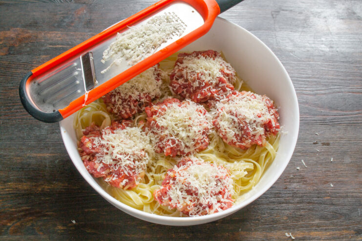 Topping the Stuffed Pasta Nests with Grated Cheese Sprinkling grated hard cheese over pasta nests stuffed with minced meat.