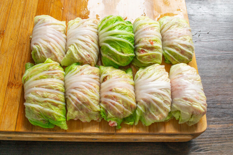 How to Roll Golubtsy Perfectly A row of neatly rolled, uncooked Napa cabbage rolls on a wooden cutting board.