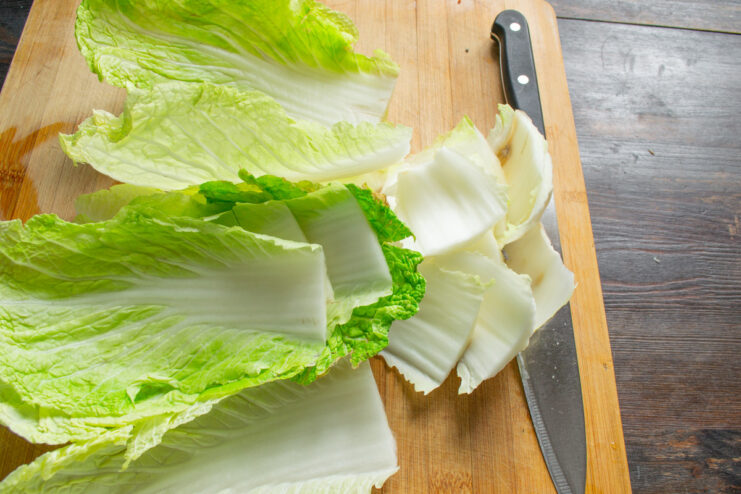 Trimming the Cabbage Leaves Before Blanching Cutting the thick white stem from the bottom of Napa cabbage leaves on a cutting board.