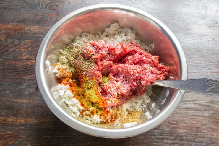Seasoning the Cabbage Roll Filling Adding spices like paprika and dried herbs to the beef and rice mixture in a bowl.