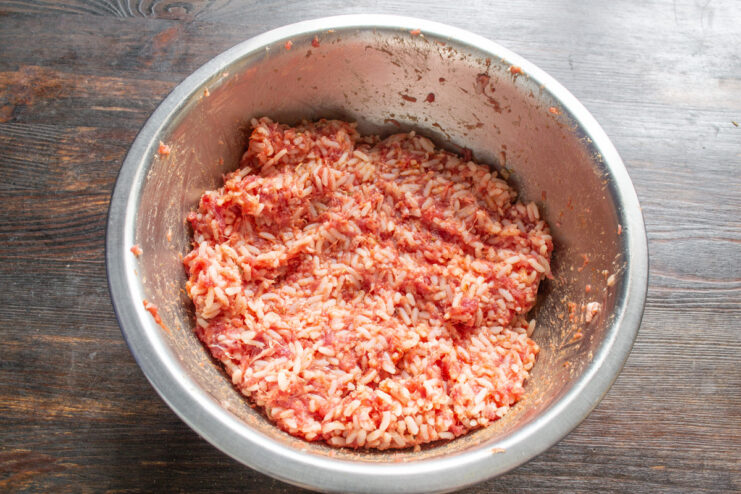 Mixing the Filling for Perfect Flavor Hands thoroughly mixing the ground beef, rice, and spices in a glass bowl.